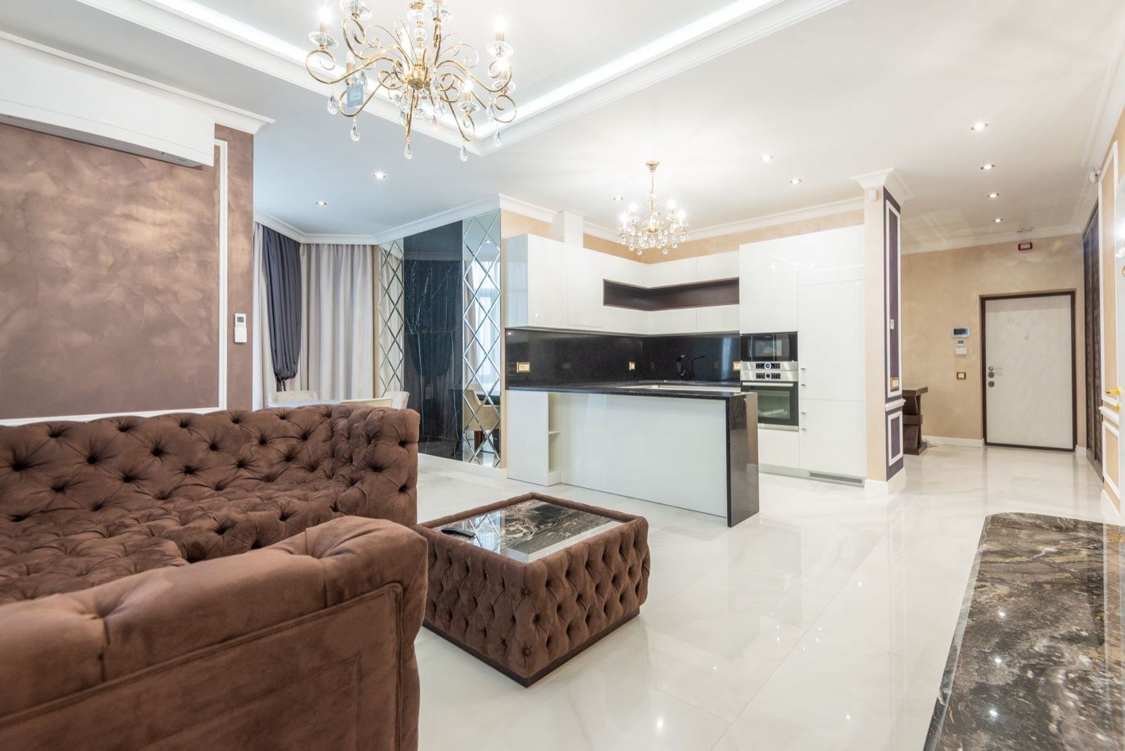 Open-plan living room with chandeliers and a mirrored kitchen